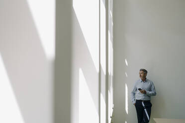 Geschäftsmann mit Blick auf das Fenster, während er sich im Büro an die Wand lehnt - JOSEF02087