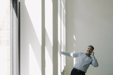 Glücklicher Geschäftsmann, der mit seinem Handy telefoniert und an der Wand im Büro hängt - JOSEF02088