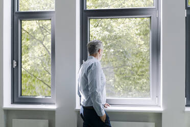 Man looking through window while standing at office - JOSEF02091