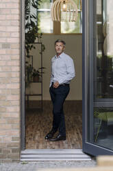 Businessman looking up while standing by door at office - JOSEF02099