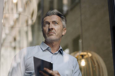 Man using digital tablet while standing by glass wall at office - JOSEF02116