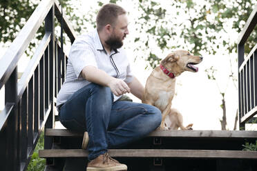 Mittlerer erwachsener Mann sitzt mit Hund auf einer Treppe im Freien - EYAF01321