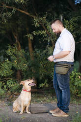 Mid adult man standing with pet dog in public park - EYAF01324