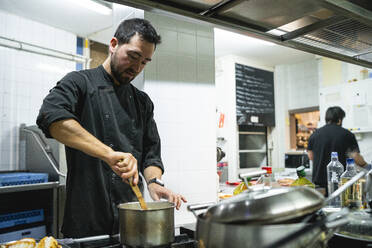 Chef preparing food with coworker working in background at kitchen - SNF00542