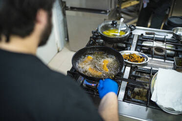 Koch brät Essen in einer Pfanne, während er am Küchentisch steht - SNF00548