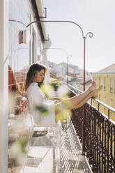 Young woman relaxing on sunny apartment balcony, Lisbon, Portugal - FSIF05156