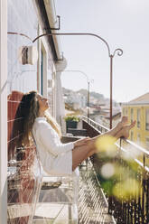 Gelassene junge Frau entspannt sich auf dem sonnigen Balkon ihrer Wohnung, Lissabon, Portugal - FSIF05159