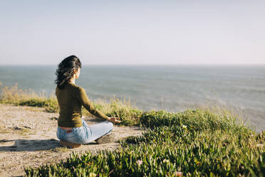 Serene woman meditating on sunny cliff overlooking sea - FSIF05163