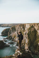 Männlicher Fotograf auf einer malerischen Meeresklippe, Bedruthan Steps, Cornwall, UK - FSIF05173