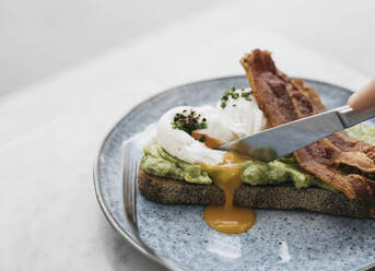 Knife cutting through avocado toast with egg and bacon - FSIF05186