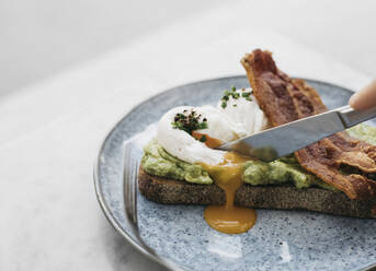 Messer schneidet durch Avocado-Toast mit Ei und Speck - FSIF05186