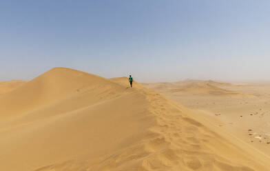 Boy walking along sunny desert sand dune ridge, Namibia - FSIF05195