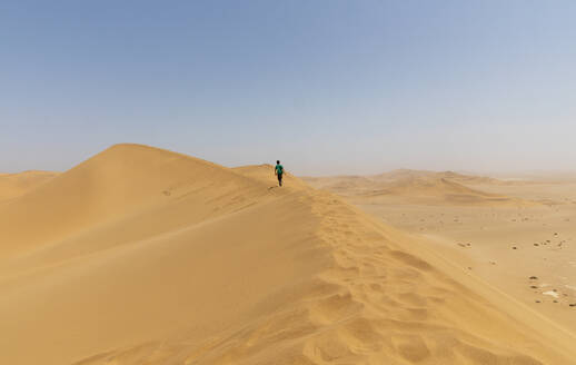 Junge wandert entlang eines sonnigen Dünenkamms in der Wüste, Namibia - FSIF05195