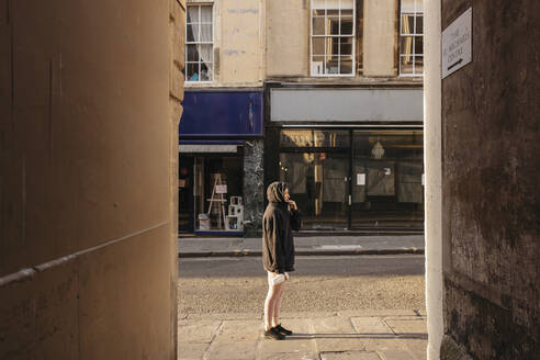 Junge Frau im Kapuzenpulli auf einer sonnigen, leeren Straße, Bath, Somerset, UK - FSIF05249