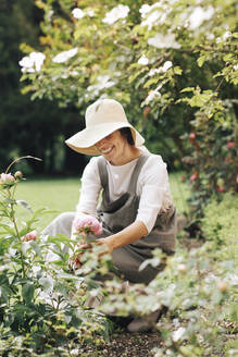 Woman smiling while picking rose flower in garden - ALBF01581