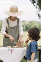 Woman cutting slice of bread for boy on table in the garden - ALBF01588