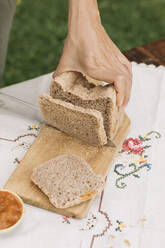 Female hand cutting bread on cutting board in garden - ALBF01589