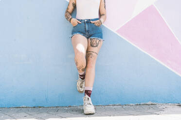 Young woman with hands in pockets standing against multi colored wall - DAMF00497