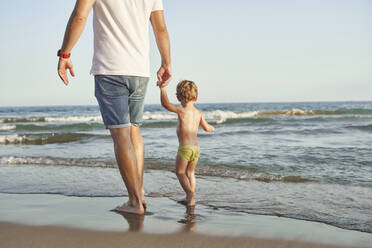 Father and son holding hands while walking at beach - VEGF02942