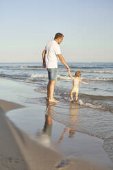 Boy holding father hand while playing in water at beach - VEGF02943
