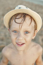 Lächelnder Junge mit Hut am Strand stehend - VEGF02951