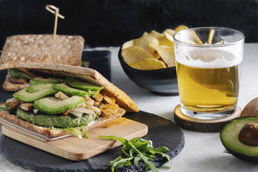 Leckeres Sandwich mit Avocado auf dem Tisch mit einem Glas Bier und Kartoffelchips im Café - ADSF15832