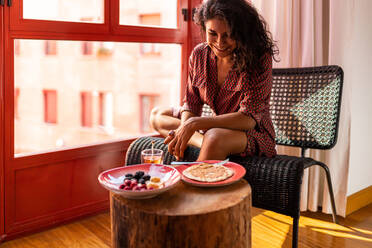 Ethnic latin woman eating healthy breakfast almond flour pancakes with berries and honey - ADSF15844