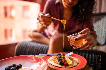 Abgeschnittene, nicht erkennbare Frau isst gesundes Frühstück Mandelmehlpfannkuchen mit Beeren und Honig - ADSF15846