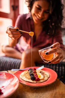 Ethnische lateinamerikanische Frau isst gesundes Frühstück Mandelmehlpfannkuchen mit Beeren und Honig - ADSF15847