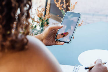 Unerkennbare afroamerikanische Frau sitzt am Tisch in einem Café und chattet auf sozialen Medien, während sie sich am Wochenende in der Stadt entspannt - ADSF15871