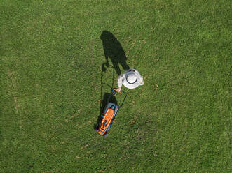 Woman with lawn mower standing in back yard - KNTF05467