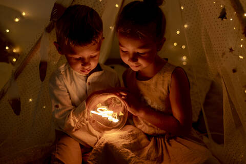 Sibling holding light while sitting in room during christmas stock photo