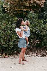 Mother and daughter kissing each other while standing in public park - EBBF00780