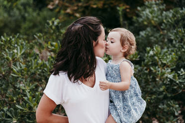 Happy mother and daughter kissing each other while standing in park - EBBF00782