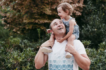 Glücklicher Vater, der seine Tochter auf der Schulter trägt, während er im Park steht - EBBF00787