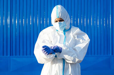 Weibliche Krankenschwester trägt Handschuh und steht an einer blauen Wand an einem sonnigen Tag - PGF00118