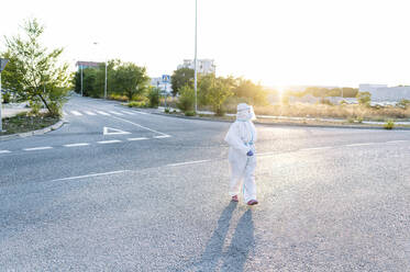 Weibliche Krankenschwester in Schutzkleidung schaut beim Gehen auf der Straße in der Stadt weg - PGF00123