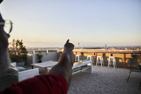 Cropped image of man pointing at clear sky from building terrace during sunset stock photo