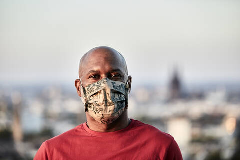 Bald man wearing protective face mask at rooftop against sky during COVID-19 stock photo