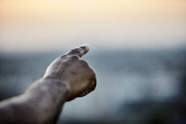 Abgeschnittene Hand eines Mannes, der von einer Gebäudeterrasse bei Sonnenuntergang in den Himmel zeigt - FMKF06450