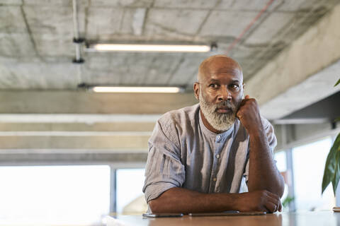 Thoughtful bald man looking away while leaning on table at rooftop stock photo