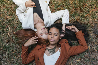 Junge multiethnische Freundinnen mit geschlossenen Augen im Gras liegend im Park - DSIF00160