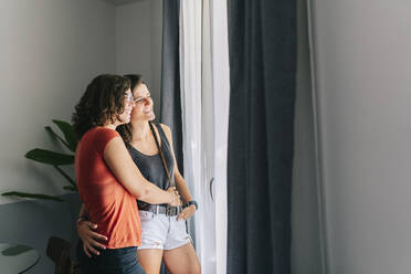 Female friends looking through window while standing at home - DGOF01508