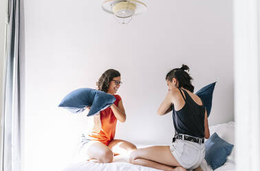 Friends enjoying pillow fight in bedroom at home - DGOF01523