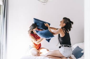 Young friends enjoying pillow fight in bedroom at home - DGOF01524