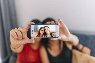 Weibliche Freunde machen ein Selfie mit dem Handy, während sie zu Hause sitzen - DGOF01528