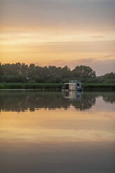 Reflecting image of houseboat in lake during sunset - MMAF01380