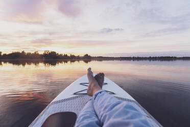 Beine einer Frau, die sich bei Sonnenuntergang auf einem Paddleboard entspannt - MMAF01387