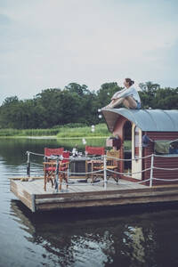 Mittlere erwachsene Frau sitzt bei Sonnenuntergang auf dem Dach eines Hausbootes - MMAF01395