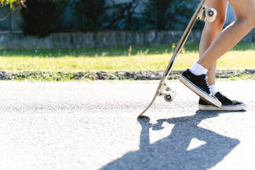 Frau hält Skateboard beim Gehen auf der Straße in der Stadt während des sonnigen Tages - FMOF01161